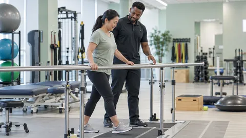 Physiotherapist helping a woman exercise at parallel bars during rehabilitation